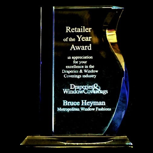 A glass award plaque with text honoring Bruce Heyman of Metropolitan Window Fashions as "Retailer of the Year" for excellence in the Draperies & Window Coverings industry.
