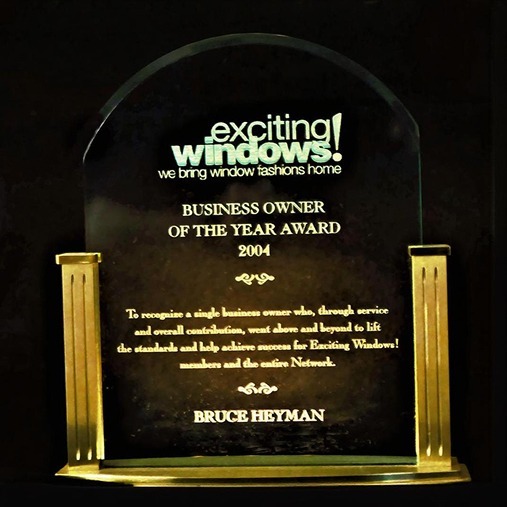 A plaque award with gold accents reads "exciting windows! BUSINESS OWNER OF THE YEAR AWARD 2004" presented to Bruce Heyman for outstanding service and contribution to the Exciting Windows! network.